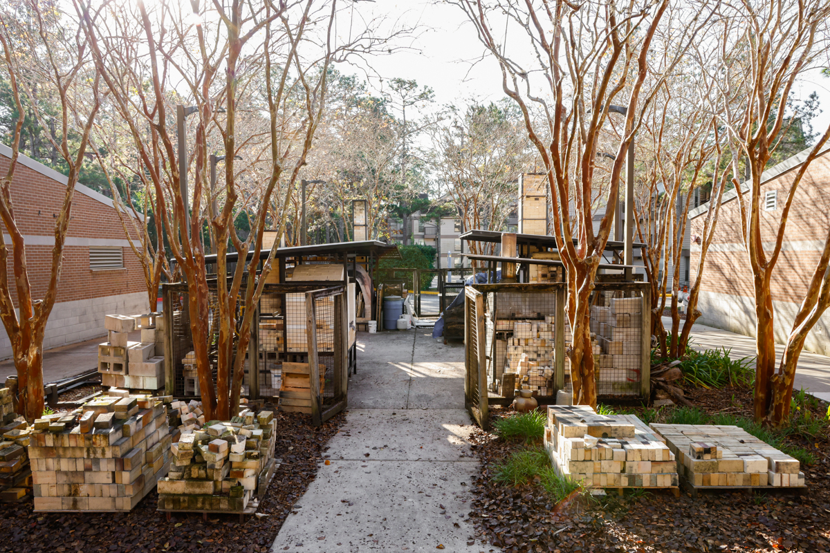 An outdoor view of a brick storage area with neatly stacked bricks and trees lining the pathway.
