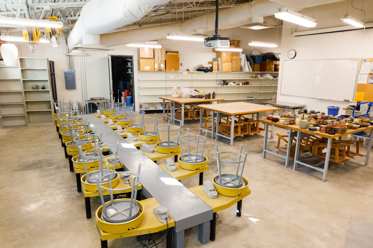 A pottery studio featuring several pottery wheels lined up and worktables filled with tools and materials.
