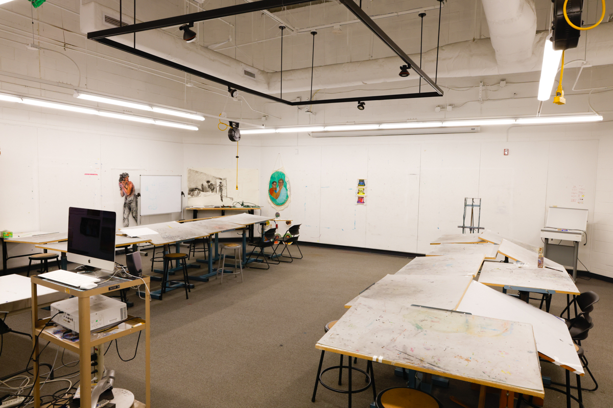 Art studio featuring several worktables and an Apple computer, with blank walls ideal for creativity and collaboration.