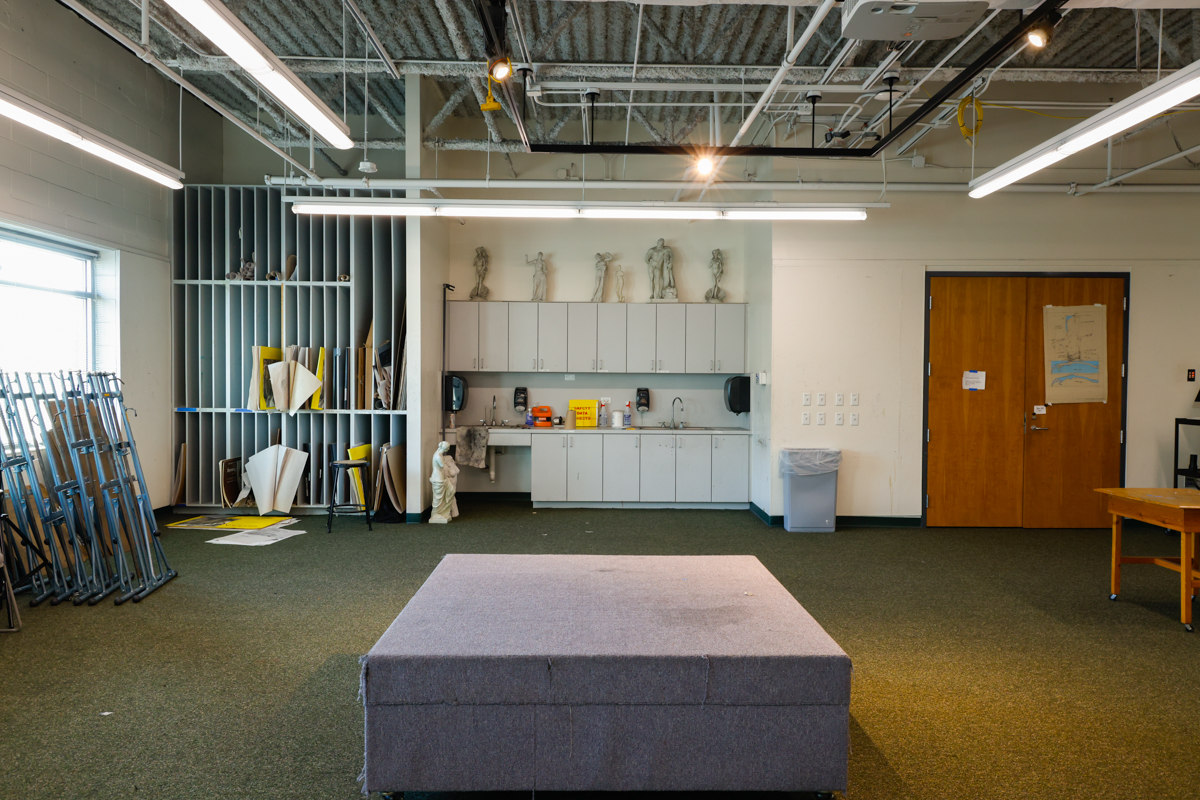 A spacious art studio featuring a gray platform, cabinets, and sculptures displayed on shelves.