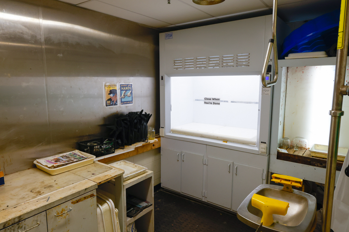 A cluttered workspace featuring a stainless steel wall, a drying station with a white enclosure, and various tools and materials, suggesting a busy environment.
