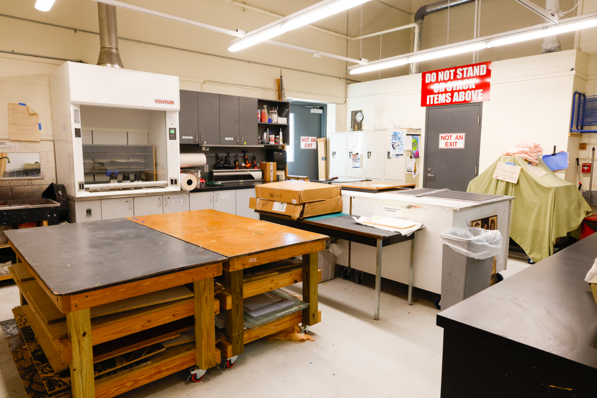 A well-lit workshop space featuring various tables, cabinets, and appliances, including a warning sign against standing under items.