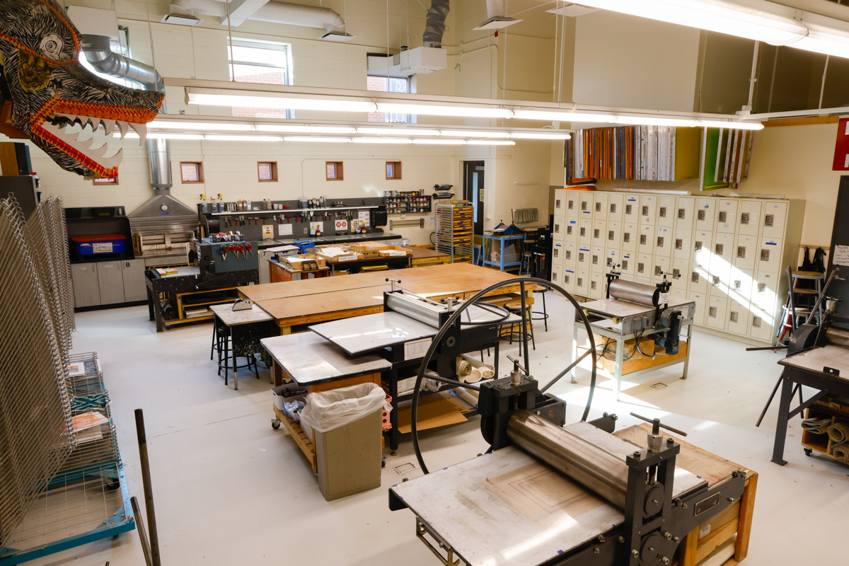 A spacious art studio featuring various workstations, printing equipment, and storage lockers, with a large dragon mural on the wall.