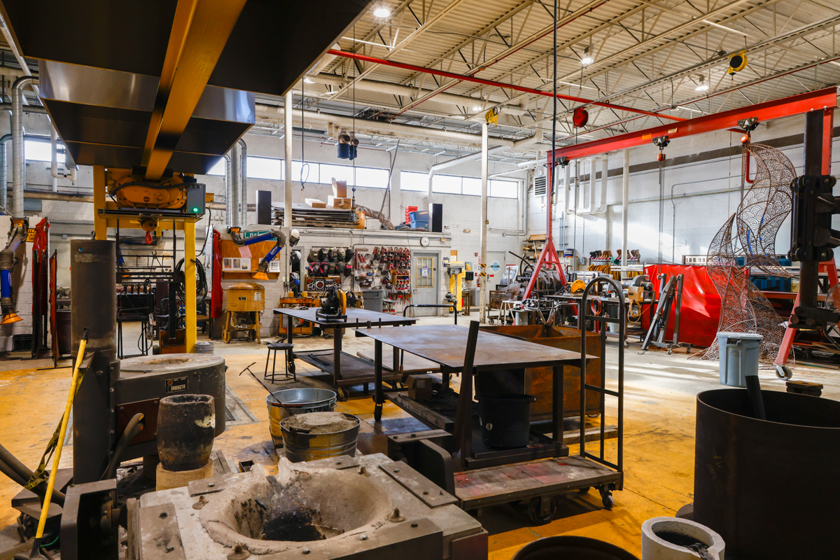 A vibrant industrial workshop filled with various tools, workstations, and equipment for metalworking and fabrication. The spacious area features bright yellow floors and a variety of machinery used in the manufacturing process.