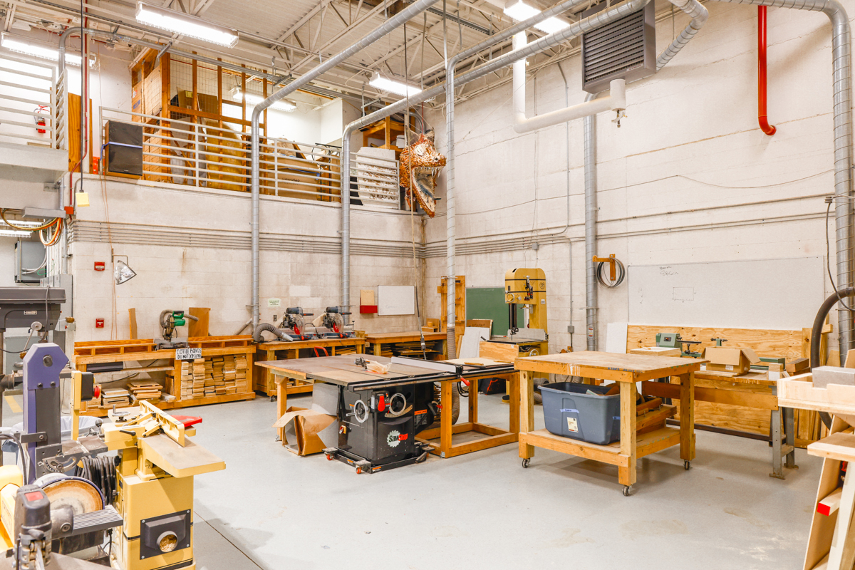 A woodworking shop displaying various tools and equipment, including a table saw and worktables, in a well-lit and organized space.