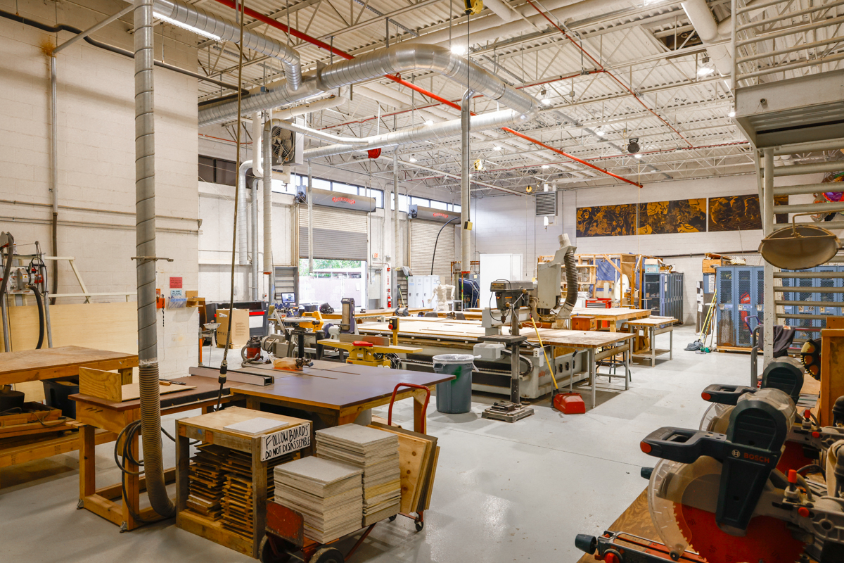 A spacious woodworking shop filled with various tools and equipment, featuring workbenches and a large saw.