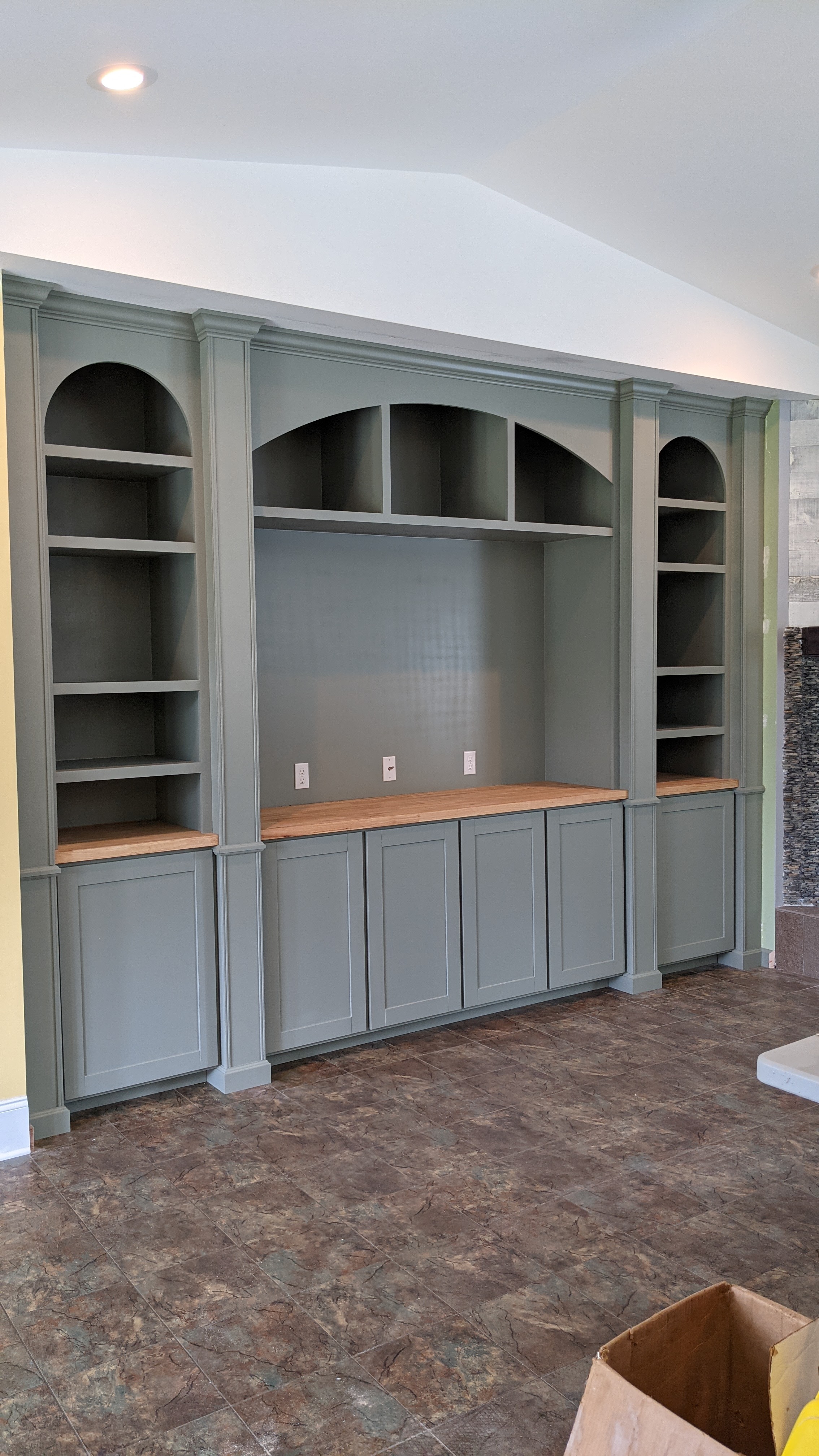 A modern, built-in shelving unit with an olive green finish, featuring open shelves and closed cabinets below against a light wall.