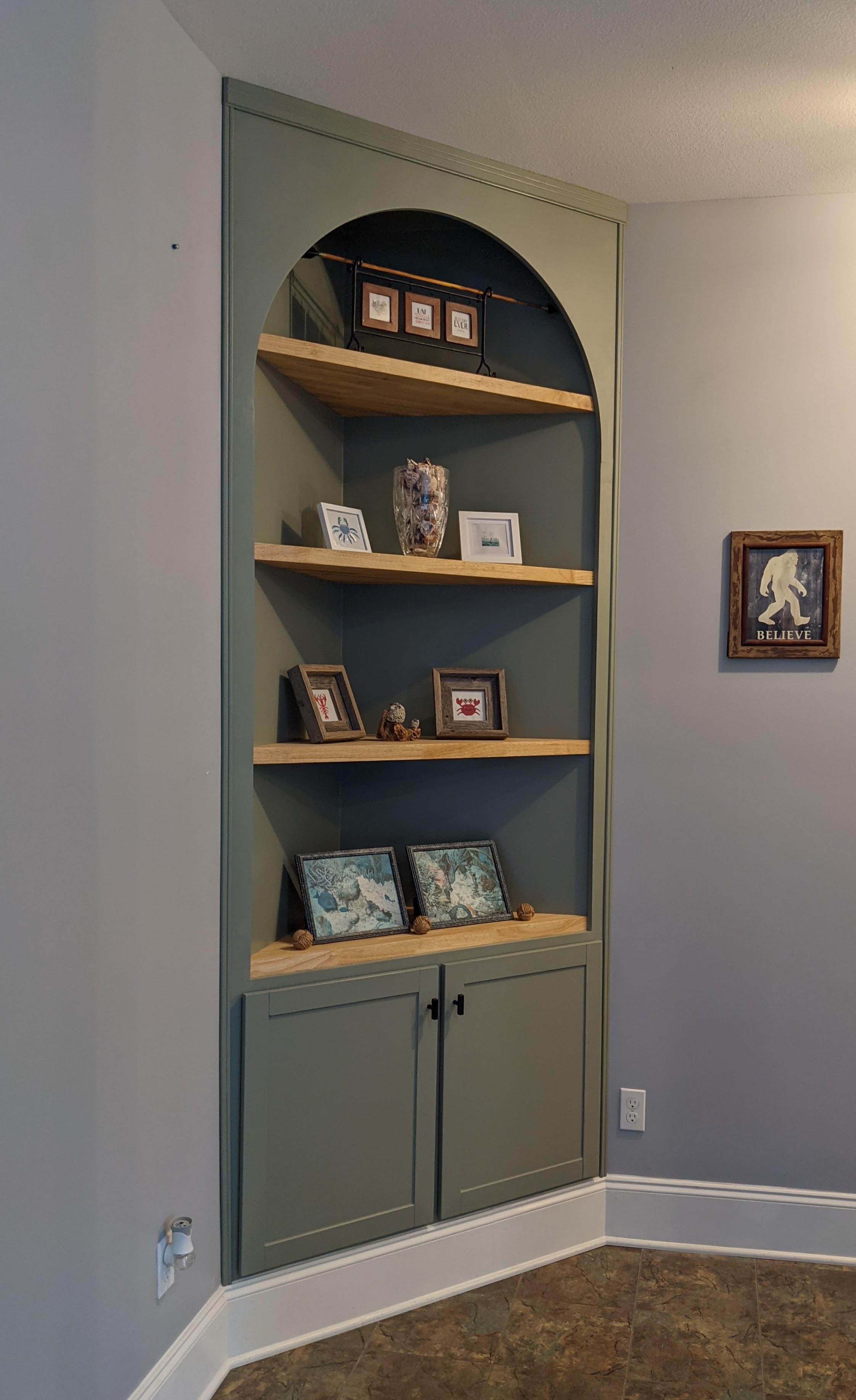A stylish green built-in shelving unit with curved top, featuring decorative items and framed photos.