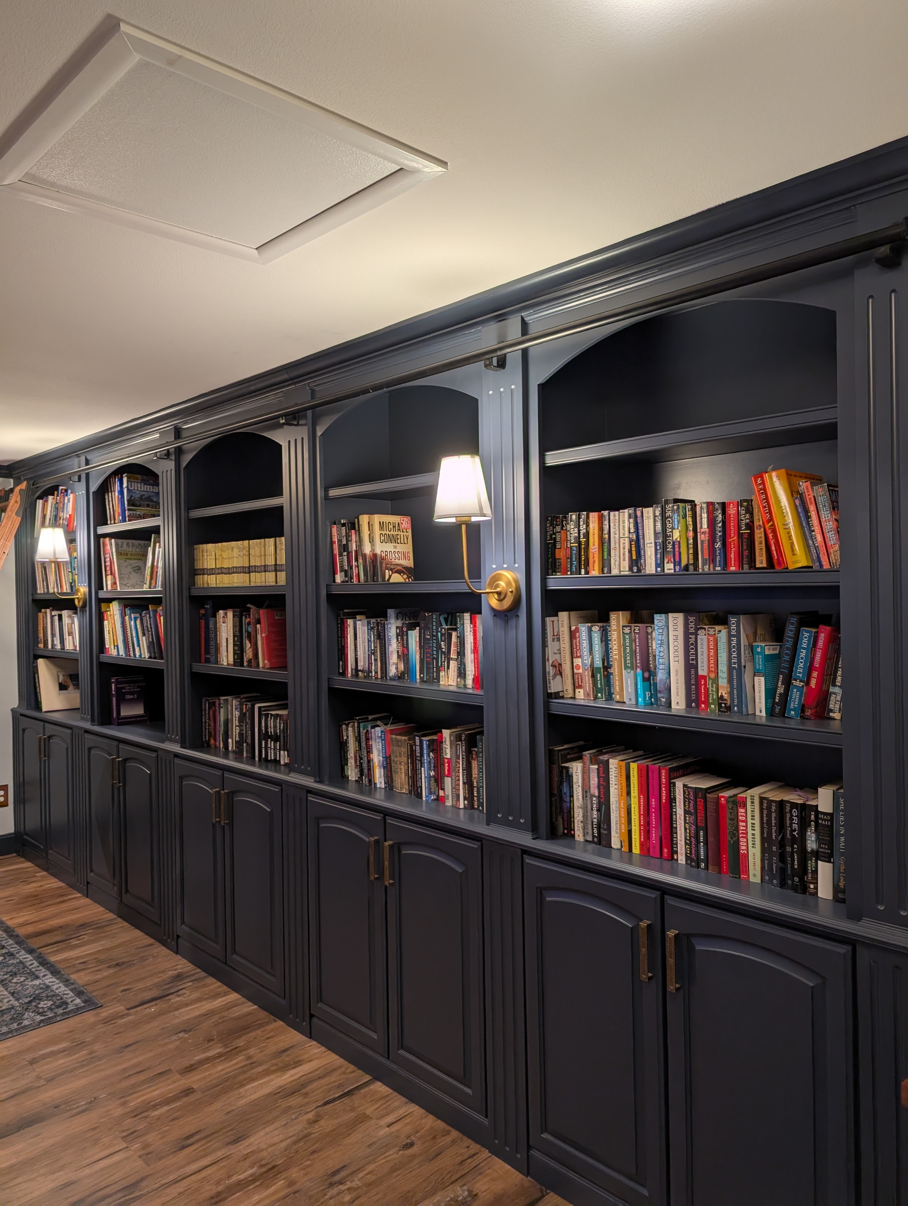 A modern dark wooden bookshelf filled with a variety of books, complemented by stylish wall sconces.