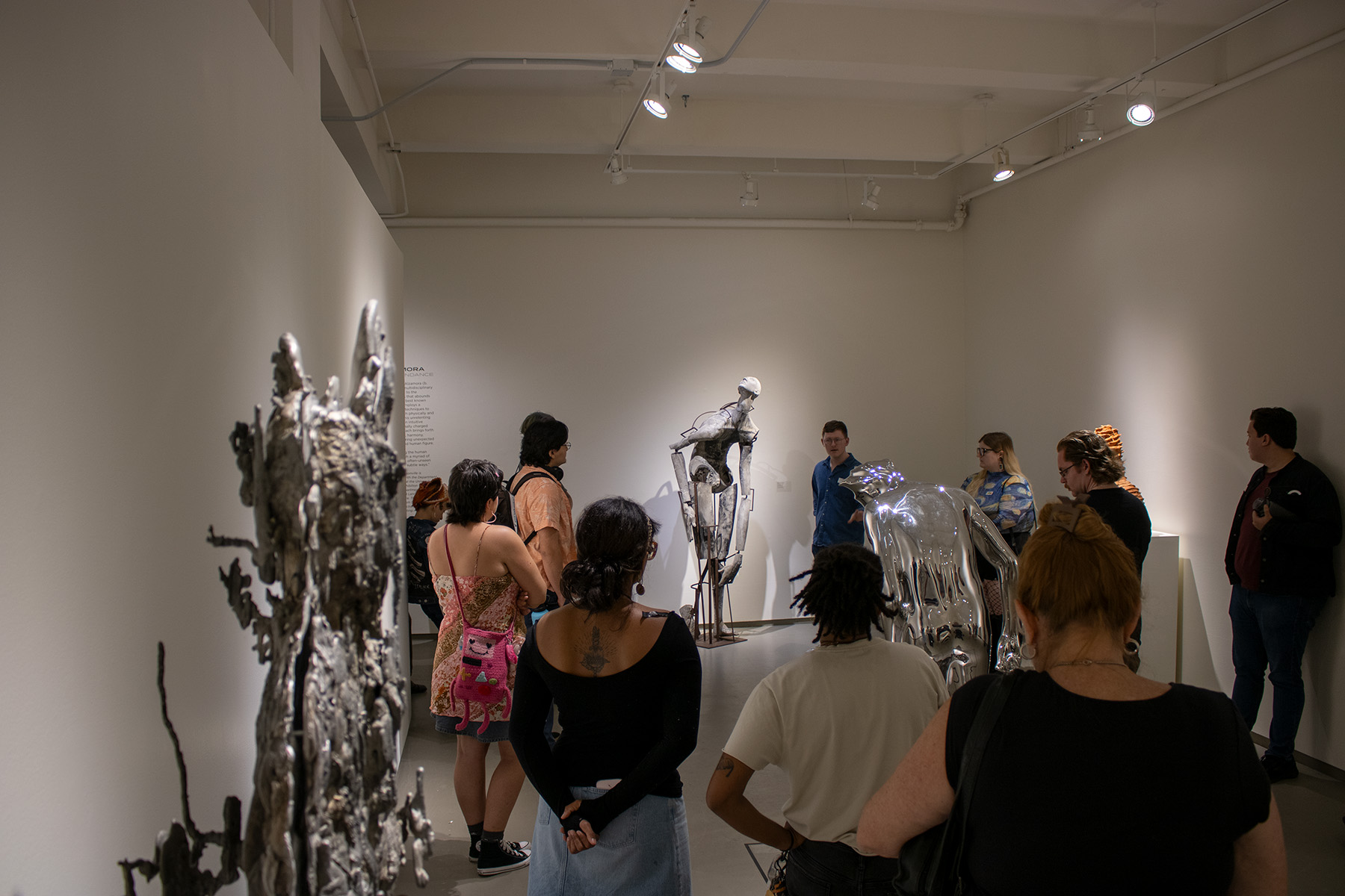 A group of people observes an art installation in an exhibition space, featuring metallic sculptures.