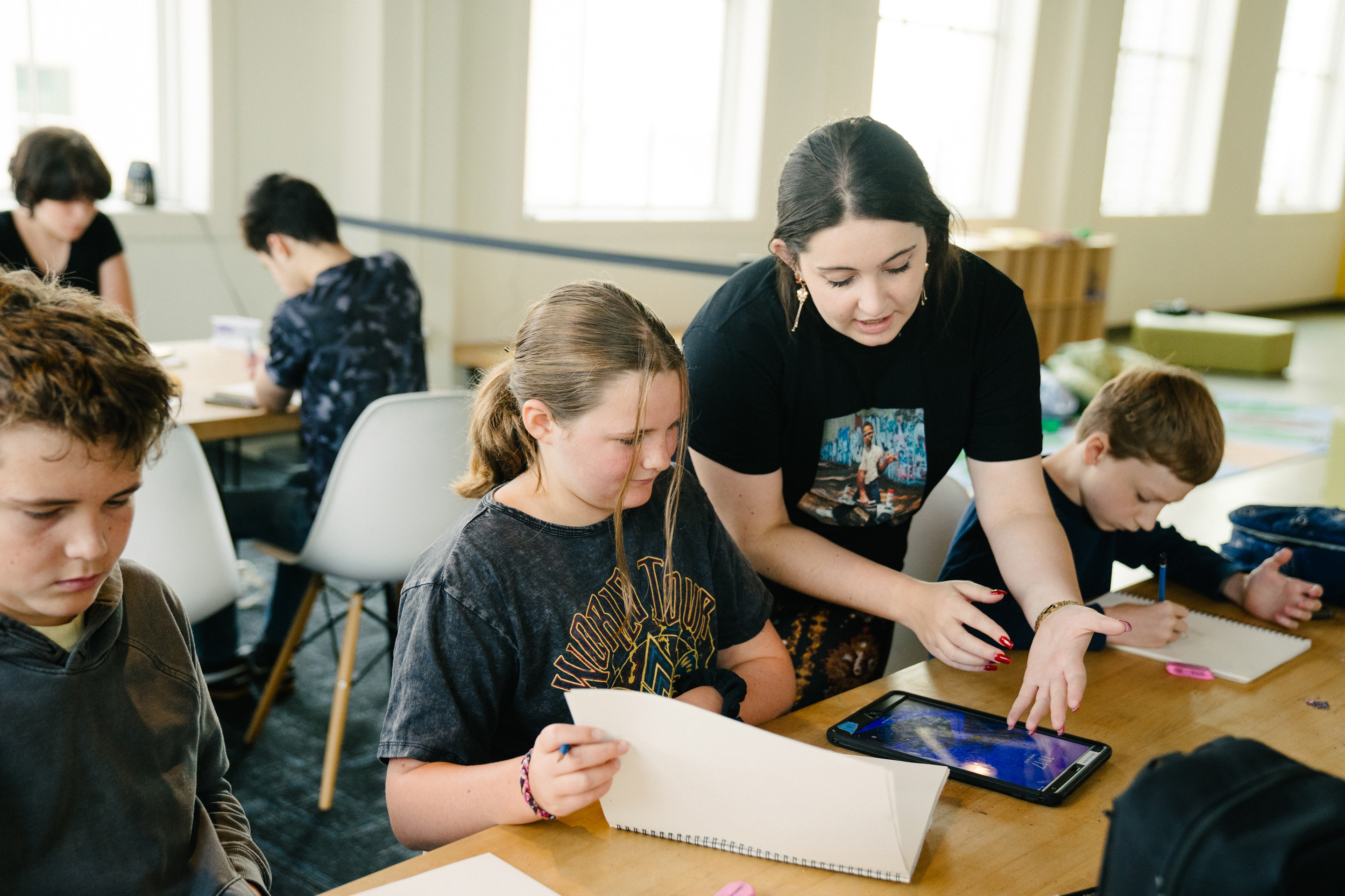 A teacher engages with students at a creative workshop, guiding them as they work on their art projects.