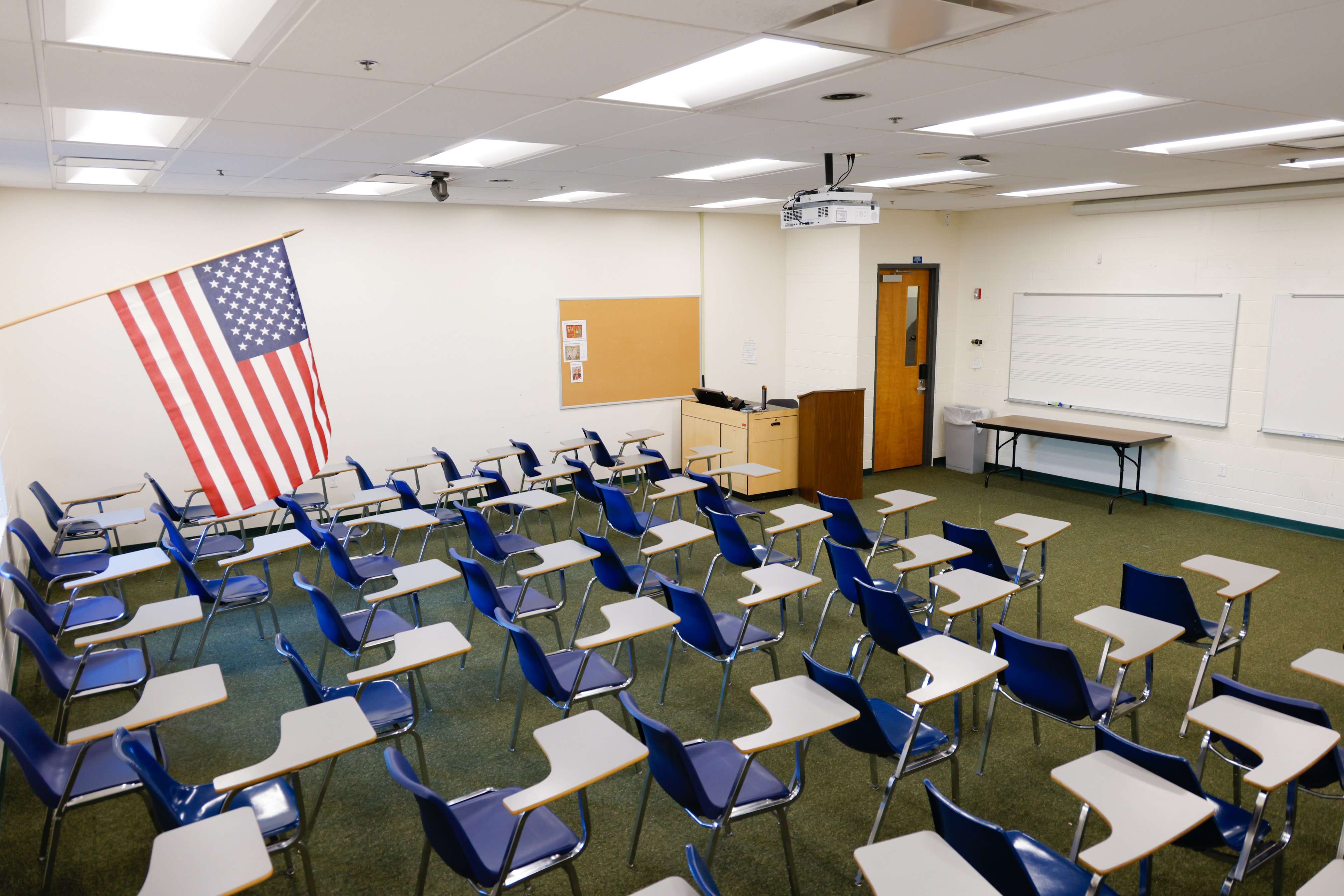 Empty classroom with American flag displayed, featuring rows of desks and a whiteboard.