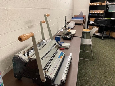 A desktop binding machine is positioned on a table in a workspace, showcasing office organization and equipment.