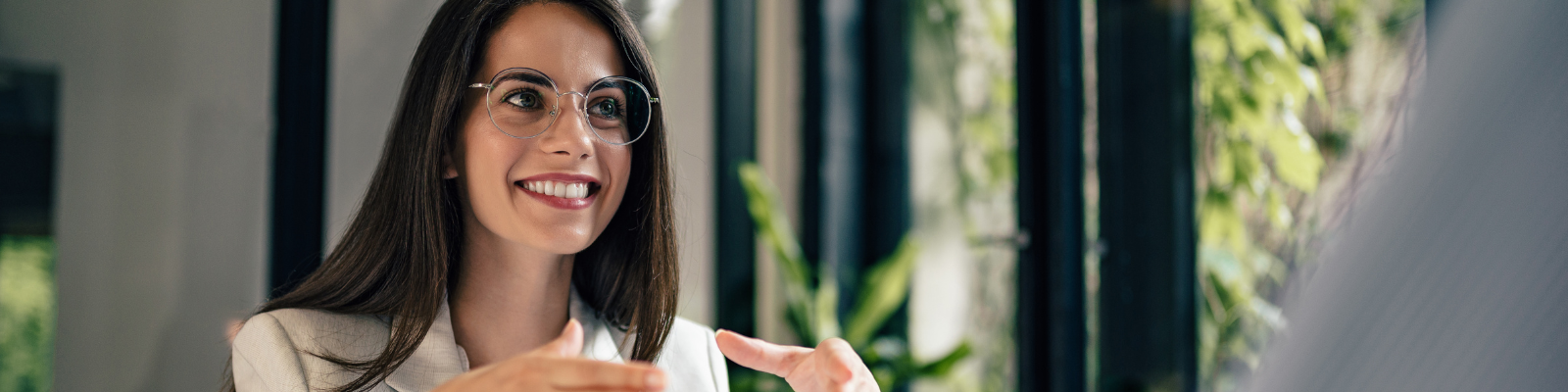 Female with brown hair and glasses sitting at a table smiling