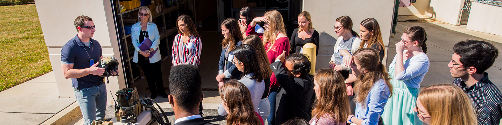 students outside in lecture with instructor showcasing military equipment