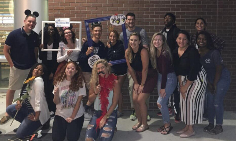 A group of students at a meeting posing with stick masks.