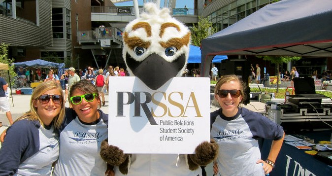 Roxie Reeve posing with fellow alumnae and ozzie holding a PRSSA sign