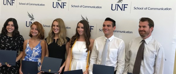 Seniors standing in front of the UNF School of Communication banner