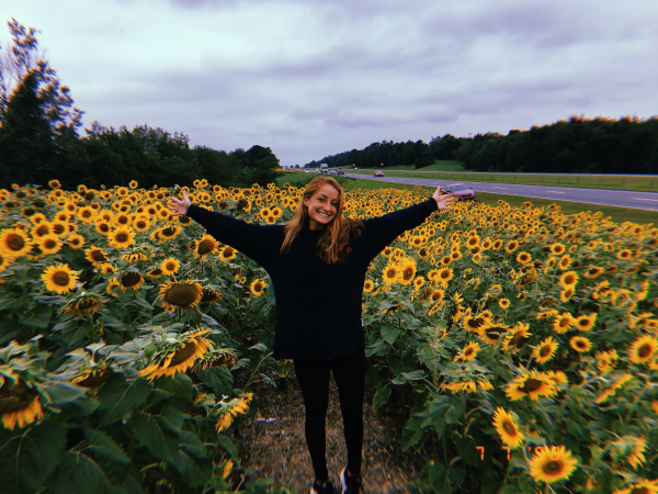 Emily Tomasello with her arms open wide in a field of sunflowers