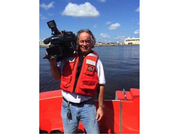 Ken Thomas poses with a camera on his shoulder on a Coast Guard ship.