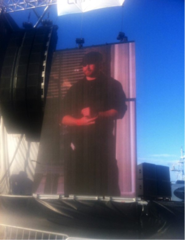 An image of Daniel Starr is projected on a screen outside.