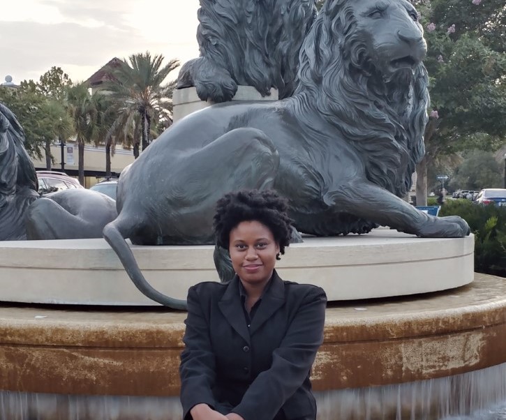 Tracey Kyles sits beside a lion statue in a city.