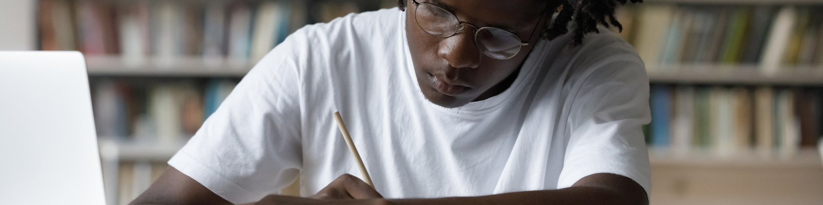 Student writing at a desk in a library setting
