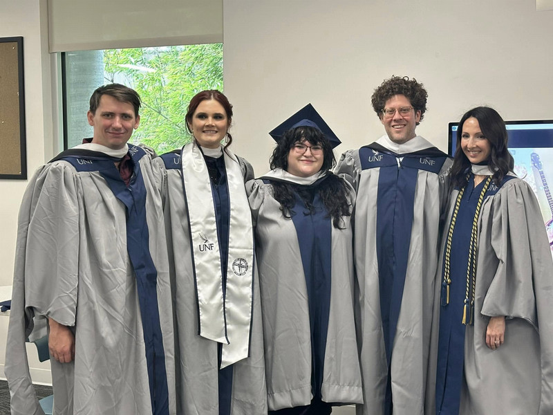 Five University of North Florida English M.A. graduates celebrate in caps and gowns on commencement day.