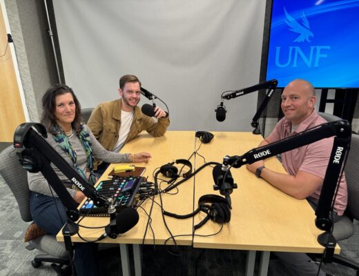 Hosts and guest recording an episode of the podcast seated at a table with microphones