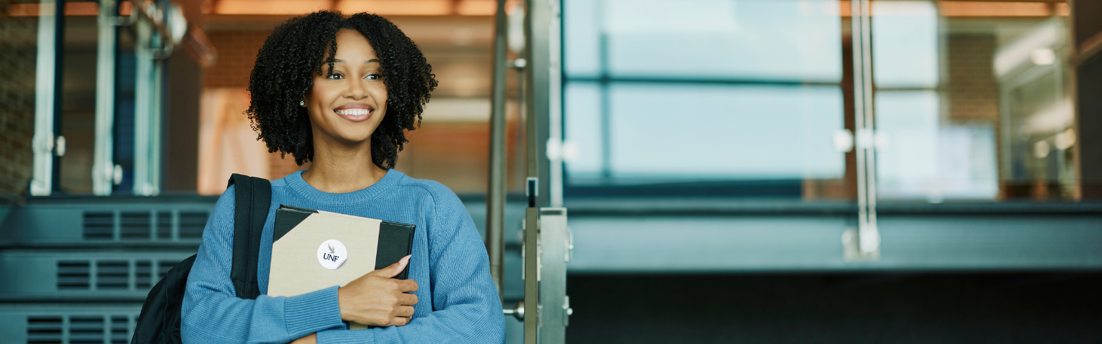 Person walking down the stairs holding a binder and wearing a backback. 