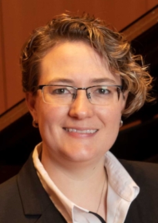 Woman with short cropped hair wearing glasses and smiling. 