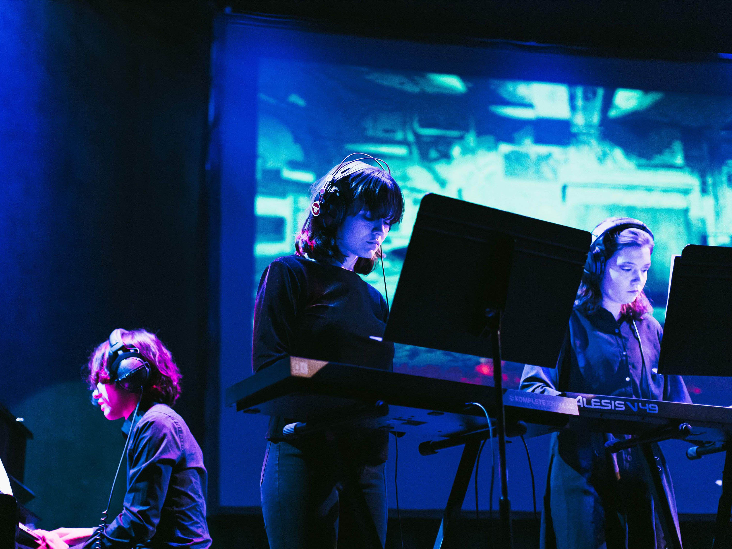 Three students wearing headphones and playing keyboards.