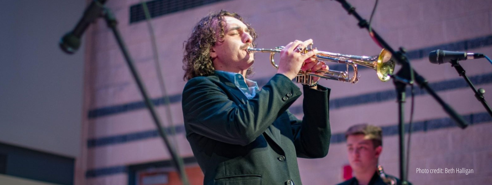 Close up of student in suit with blue shirt blowing trumpet in front of microphone