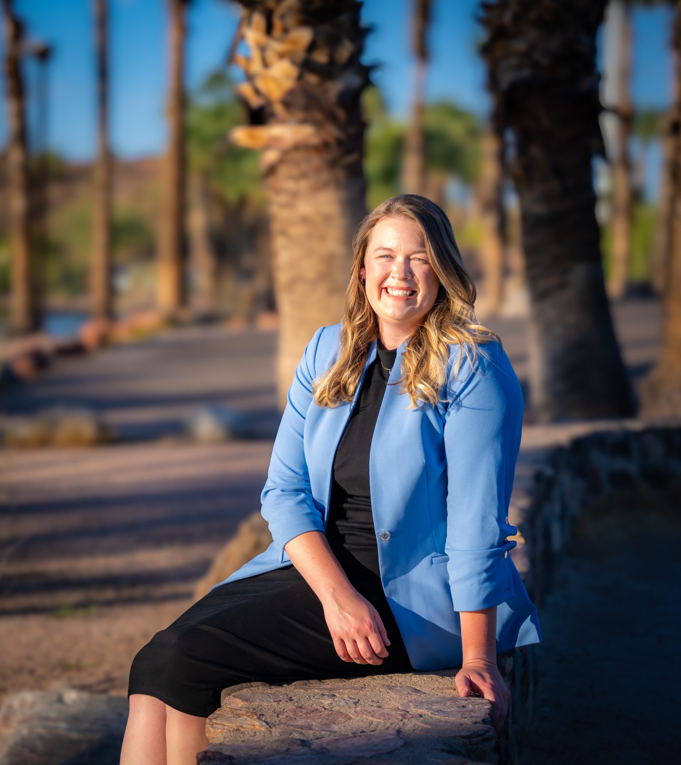 Brunette woman wearing a red dress and holding a baton. She is seated and smiling at the camera.