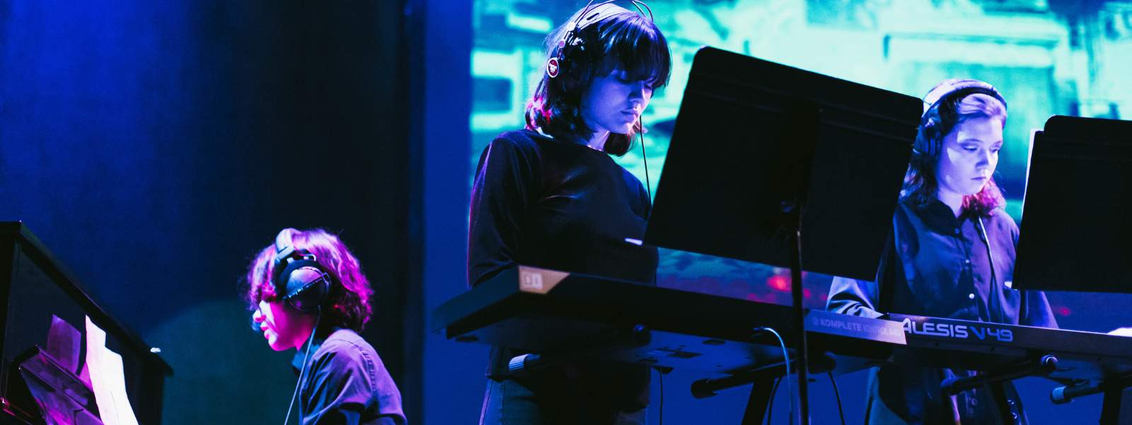 Three students wearing headphones and playing instruments