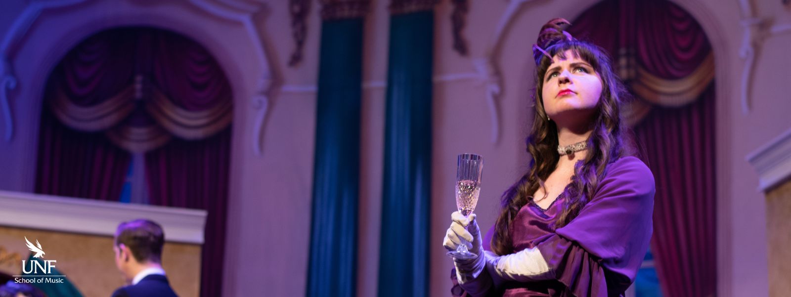 Young woman in fancy dress holding champagne glass and looking thoughtfully towards the ceiling.