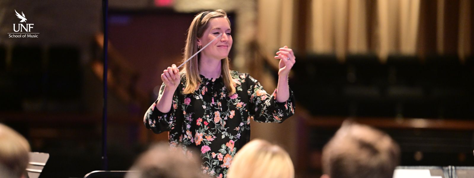 Young woman with shoulder length blonde hair holding conductor's baton and smiling.