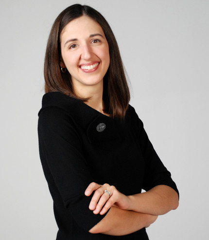 Caucasian woman with shoulder length brown hair and eyes, wearing black dress and smiling at the camera. 