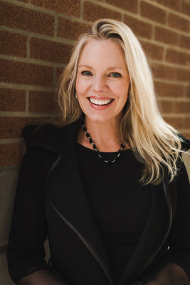 Woman with light blonde hair and bright smile leaning against brick wall. 