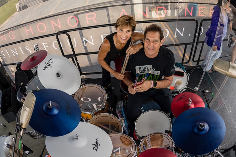 Man and woman holding drum sticks while sitting behind drum set. 