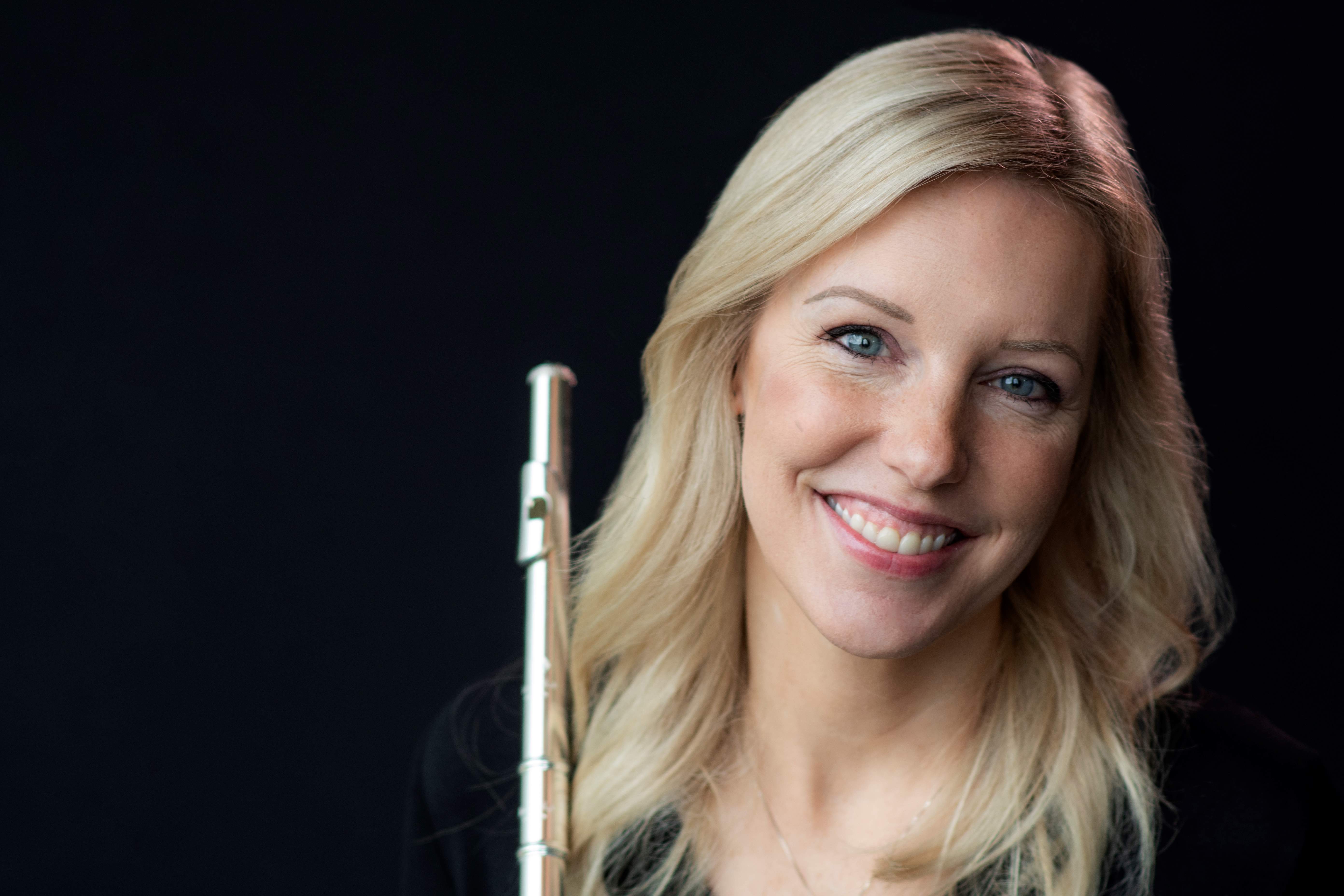 Blonde haired woman wearing a black dress, holding a flute and smiling. 