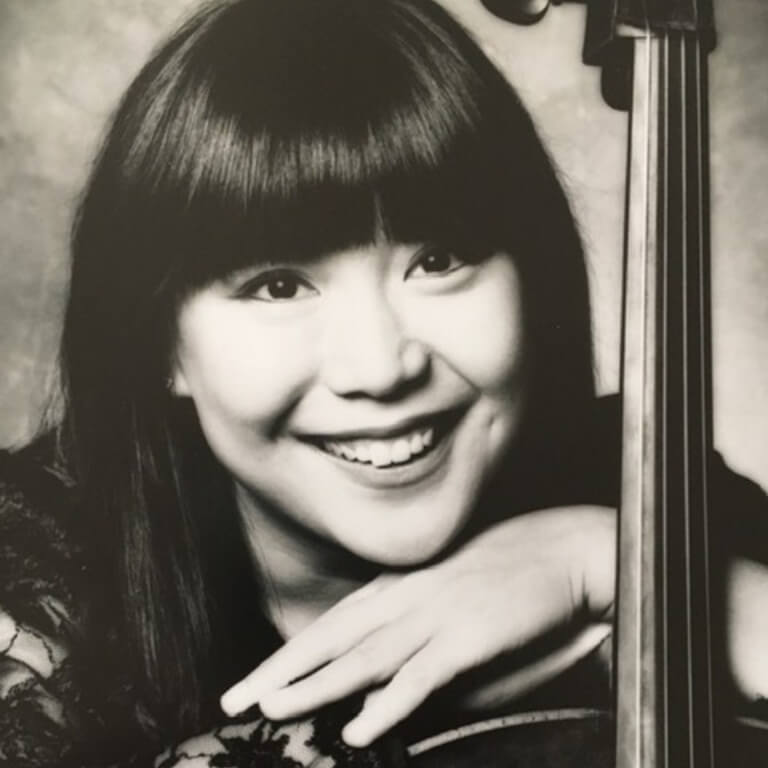 Woman with dark hair leaning against shoulder of her cello.