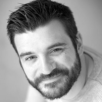 Man with full beard and short, dark hair smiling at the camera. 