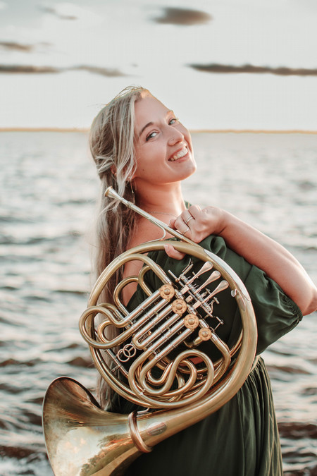 Woman in green dress standing near water and holding a horn. 