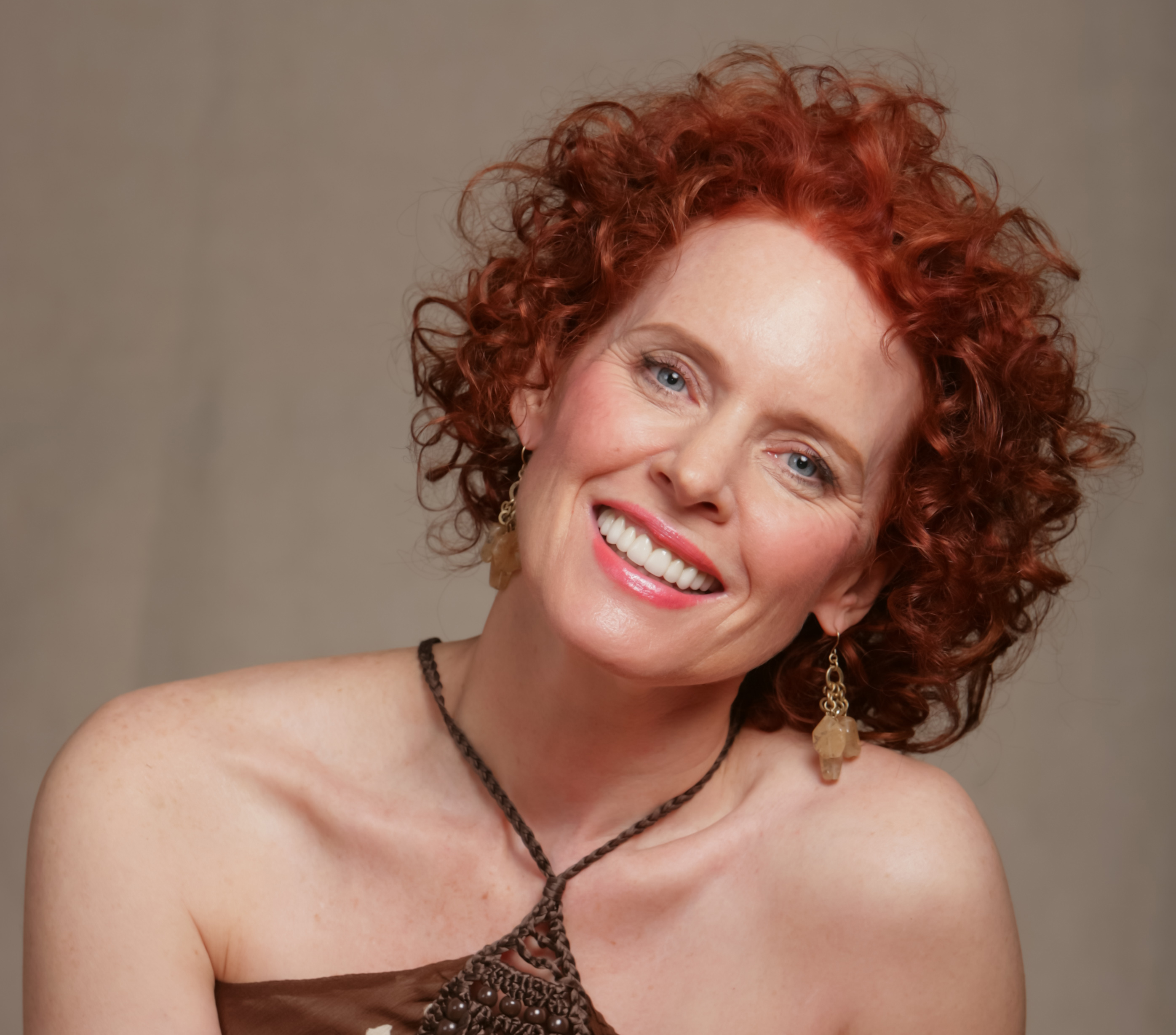 Woman with red, curly hair tilting her head and smiling. 