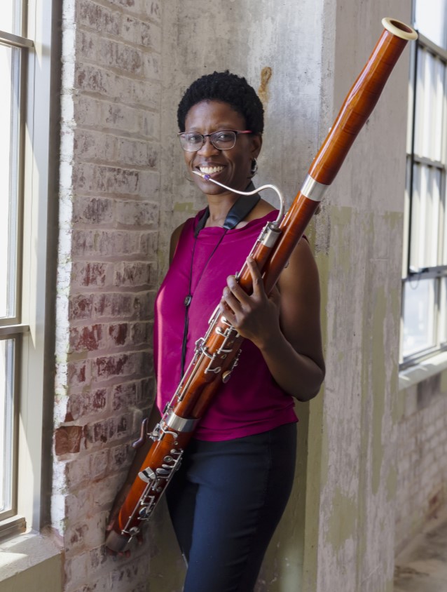 Woman with short black hair holding a bassoon and smiling.