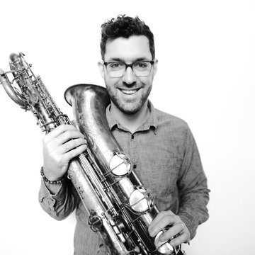 Man with short black hair wearing glasses and holding saxophone.