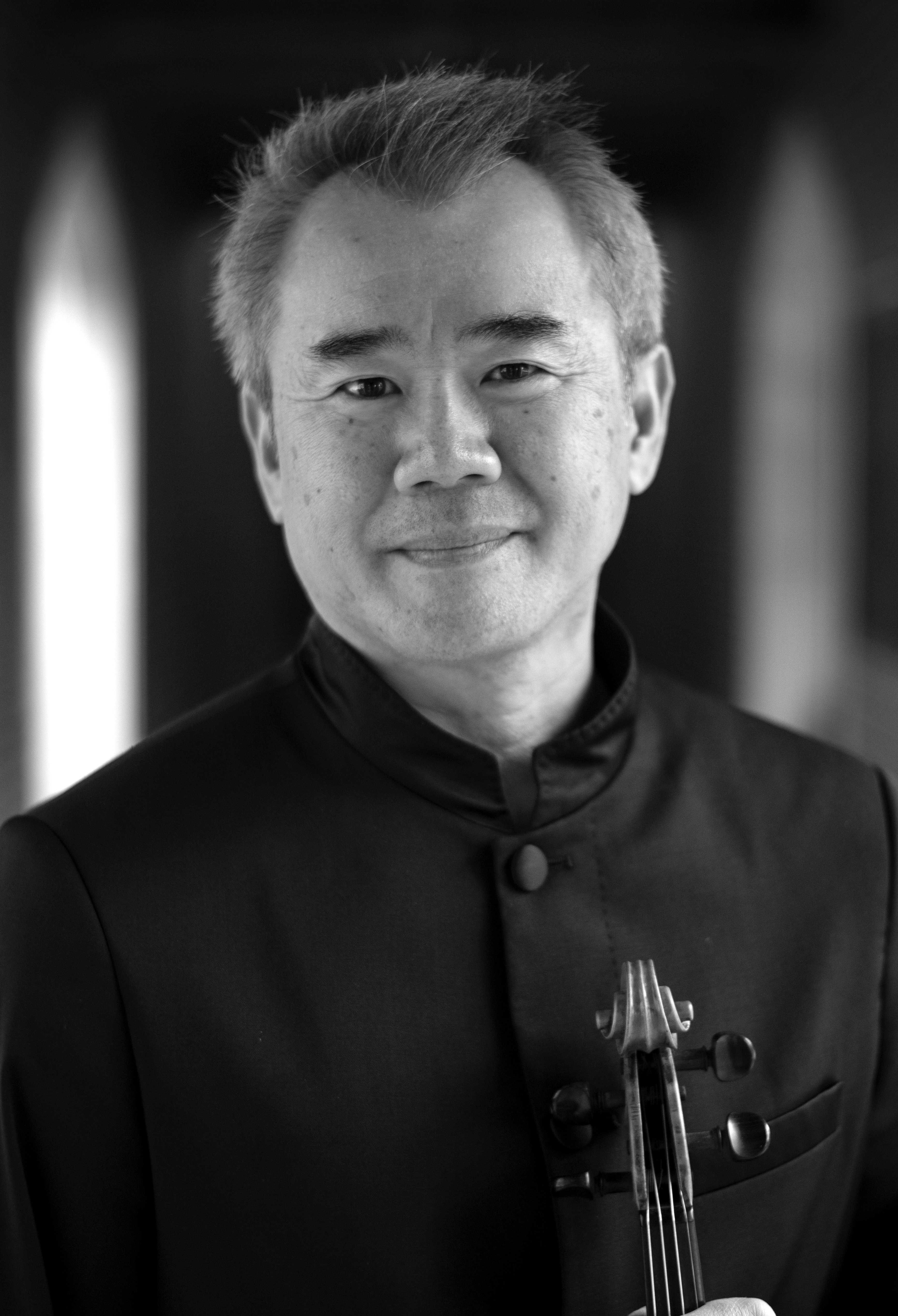 Middle-aged Asian man wearing all black suit and holding violin. He has grey hair and is smiling.