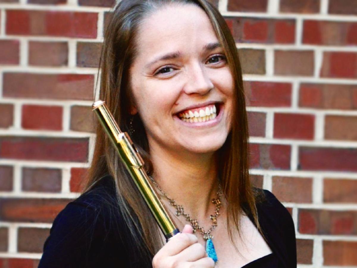 Woman with long hair holding flute and smiling.