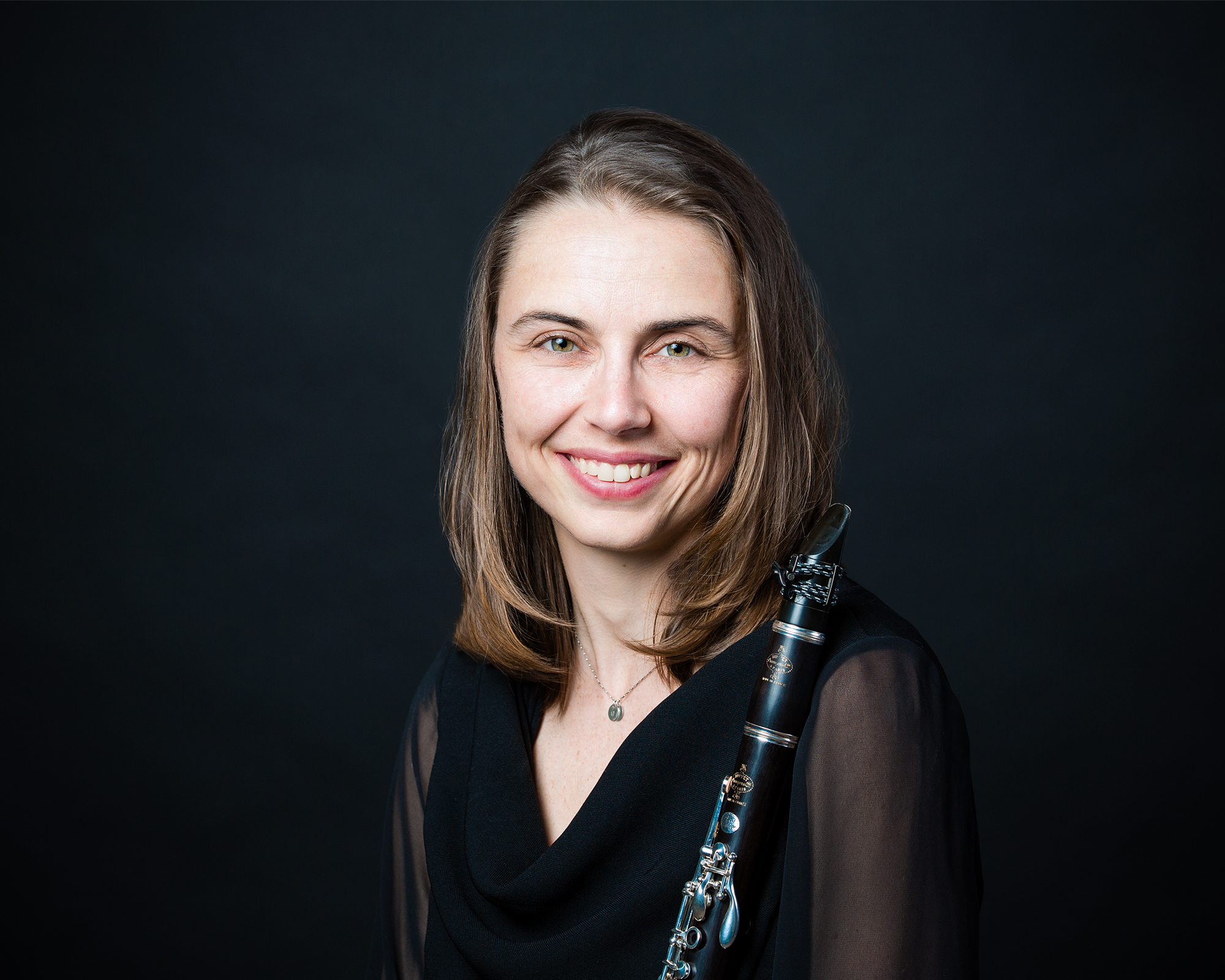 Caucasian woman with light brown, shoulder length hair smiling and holding clarinet. 